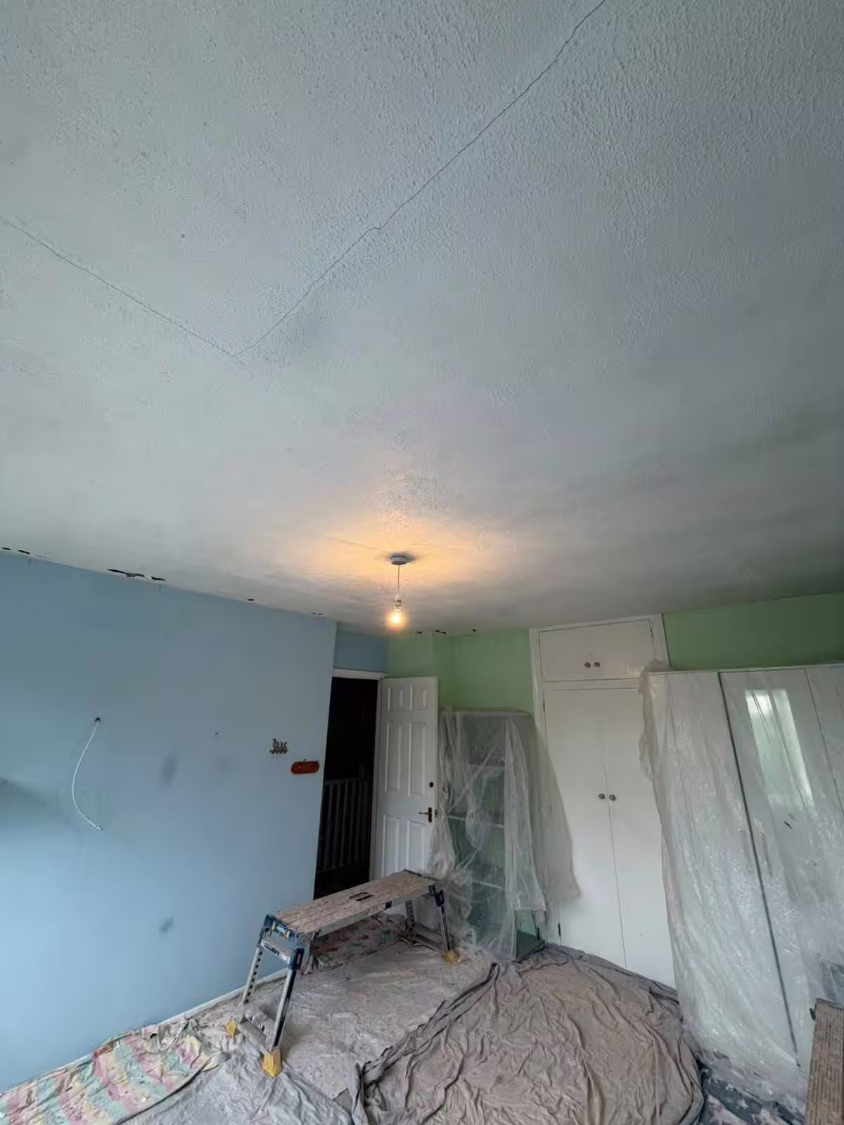 Textured ceiling with cracks running across it, the room below sheeted up